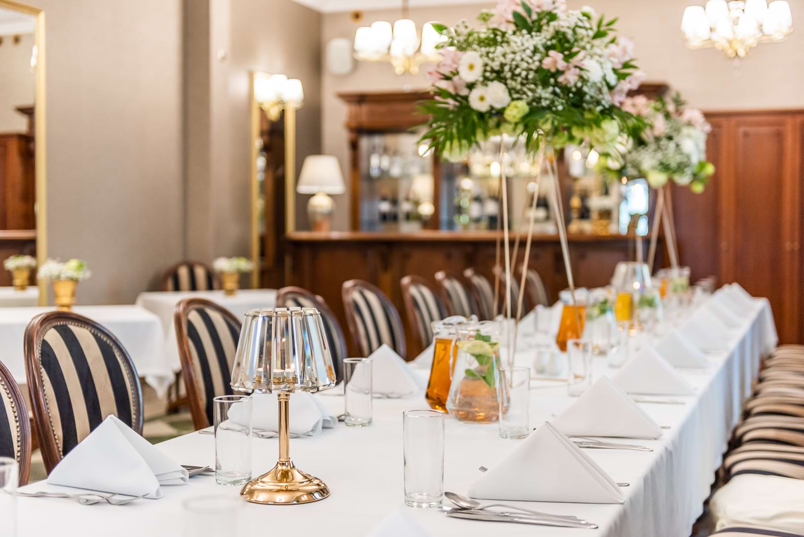 Długi stół w eleganckiej sali z kwiatową kompozycją i lampkami