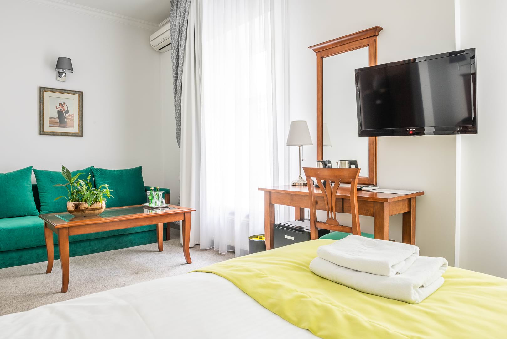 Salon hotelowy z zieloną sofą, drewnianym stolikiem i TV