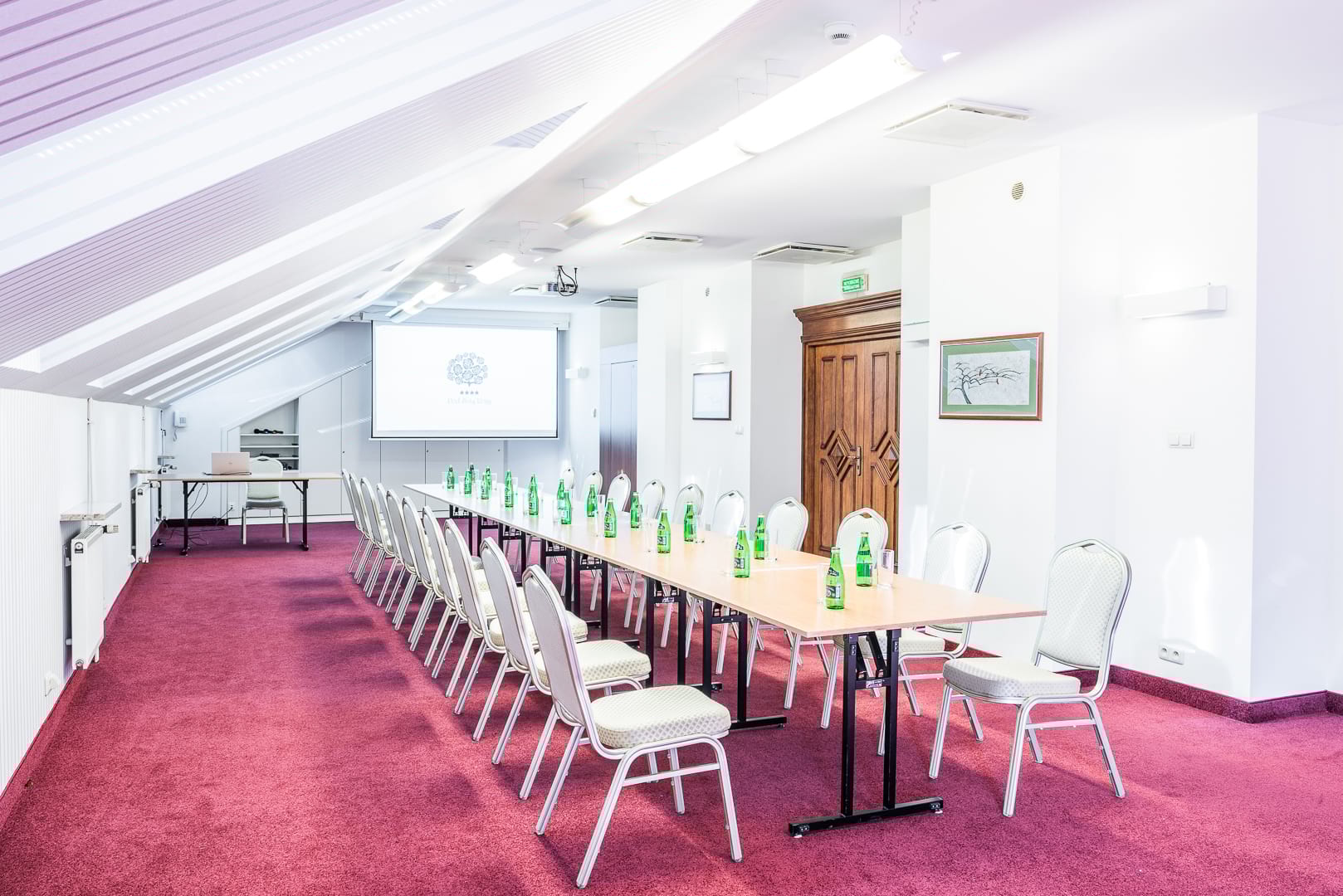 Sala konferencyjna z długim stołem, zielone butelki i ekran projekcyjny