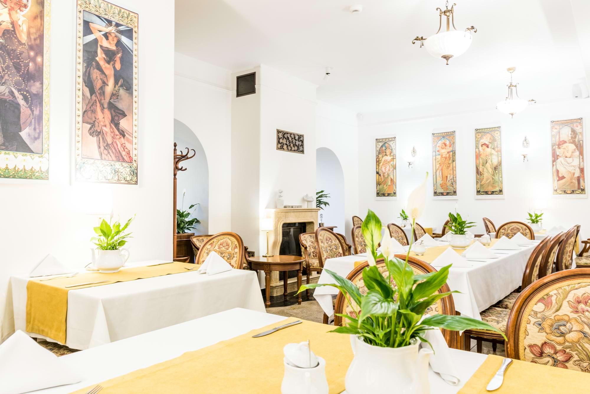 Elegancka jadalnia z białymi obrusami, żółtymi narzutami i roślinami