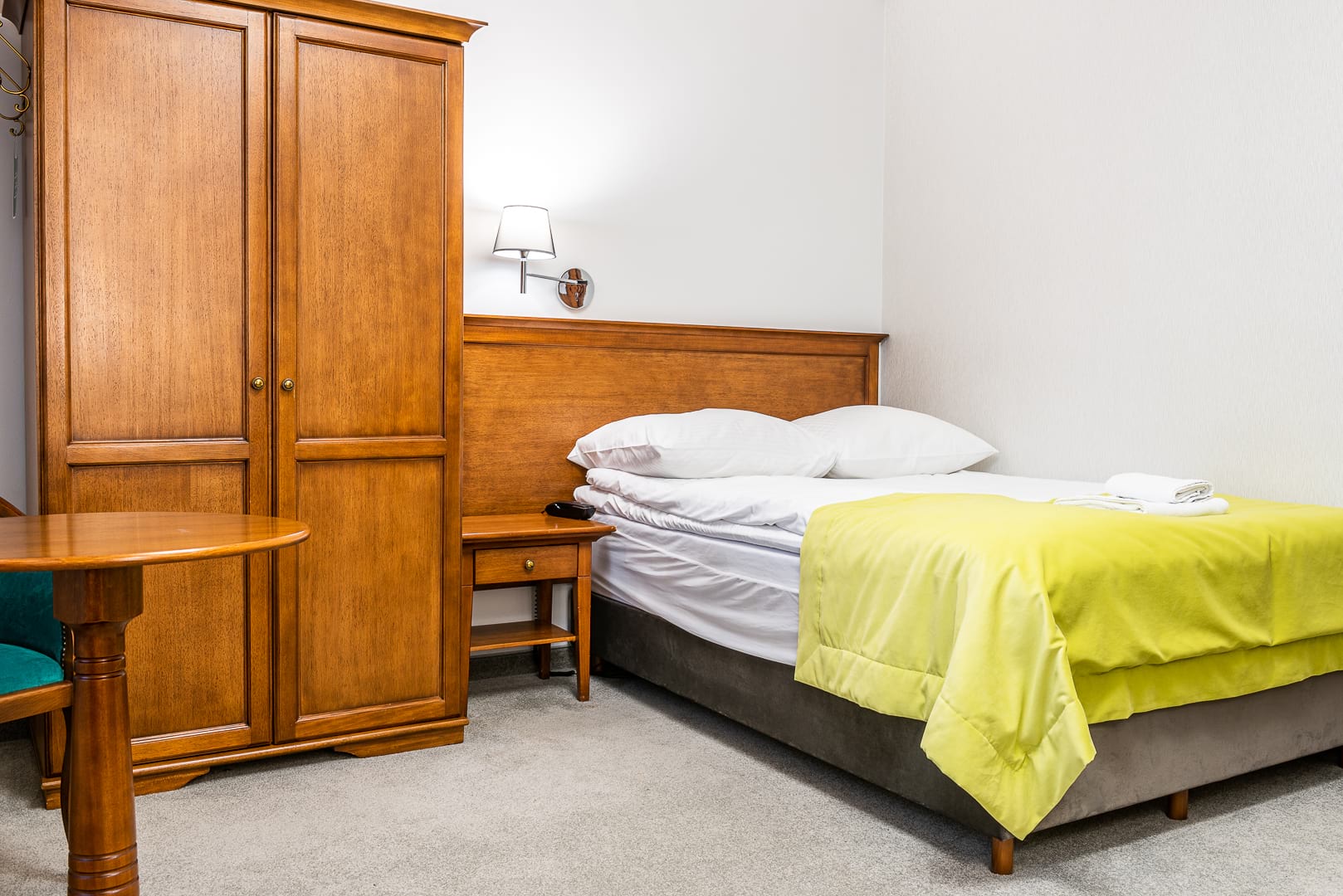Hotelowy pokój z dużą drewnianą szafą i łóżkiem z żółto-zielonym kocem