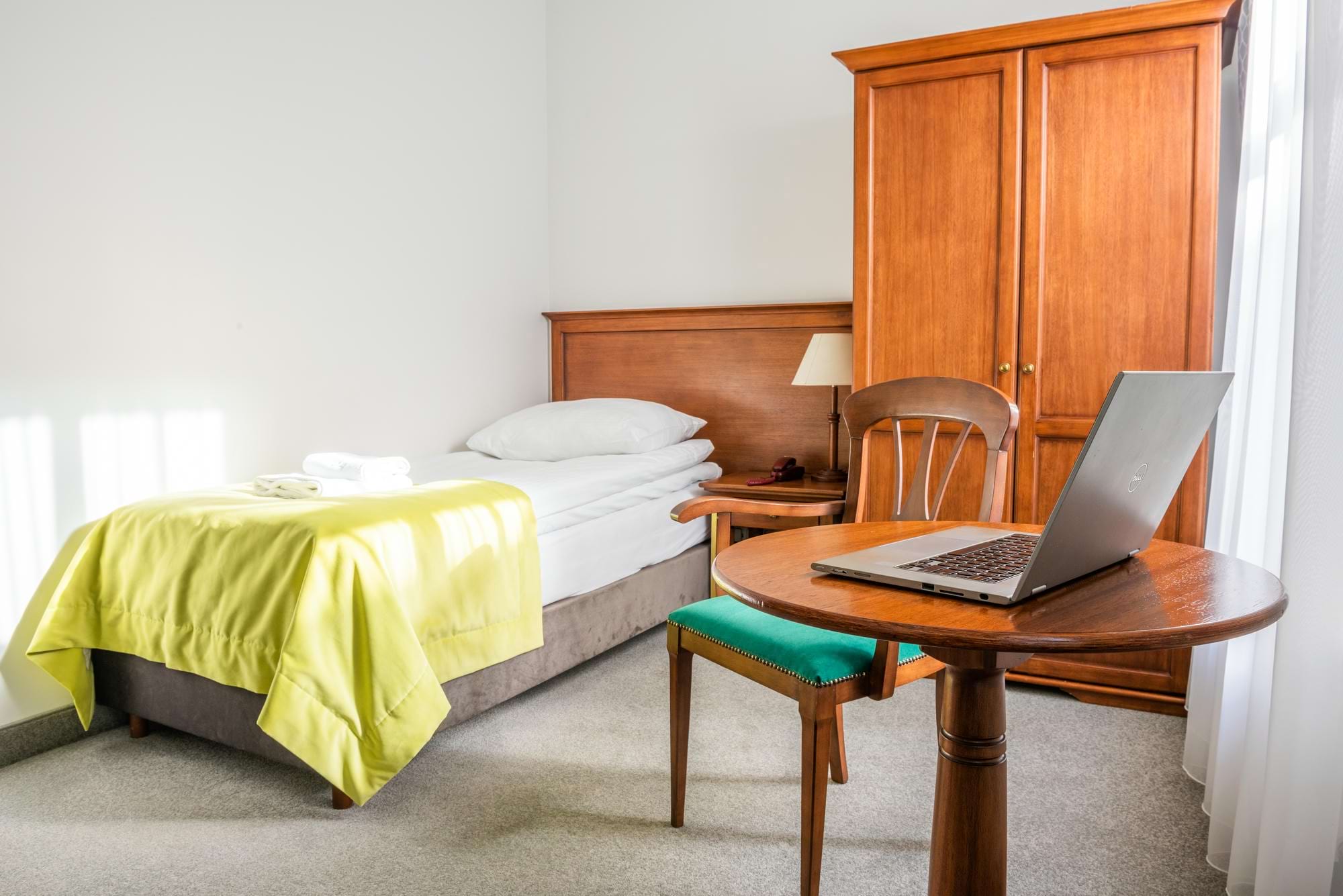 Sypialnia z łóżkiem, żółtą narzutą, drewnianą szafą i laptopem na stole