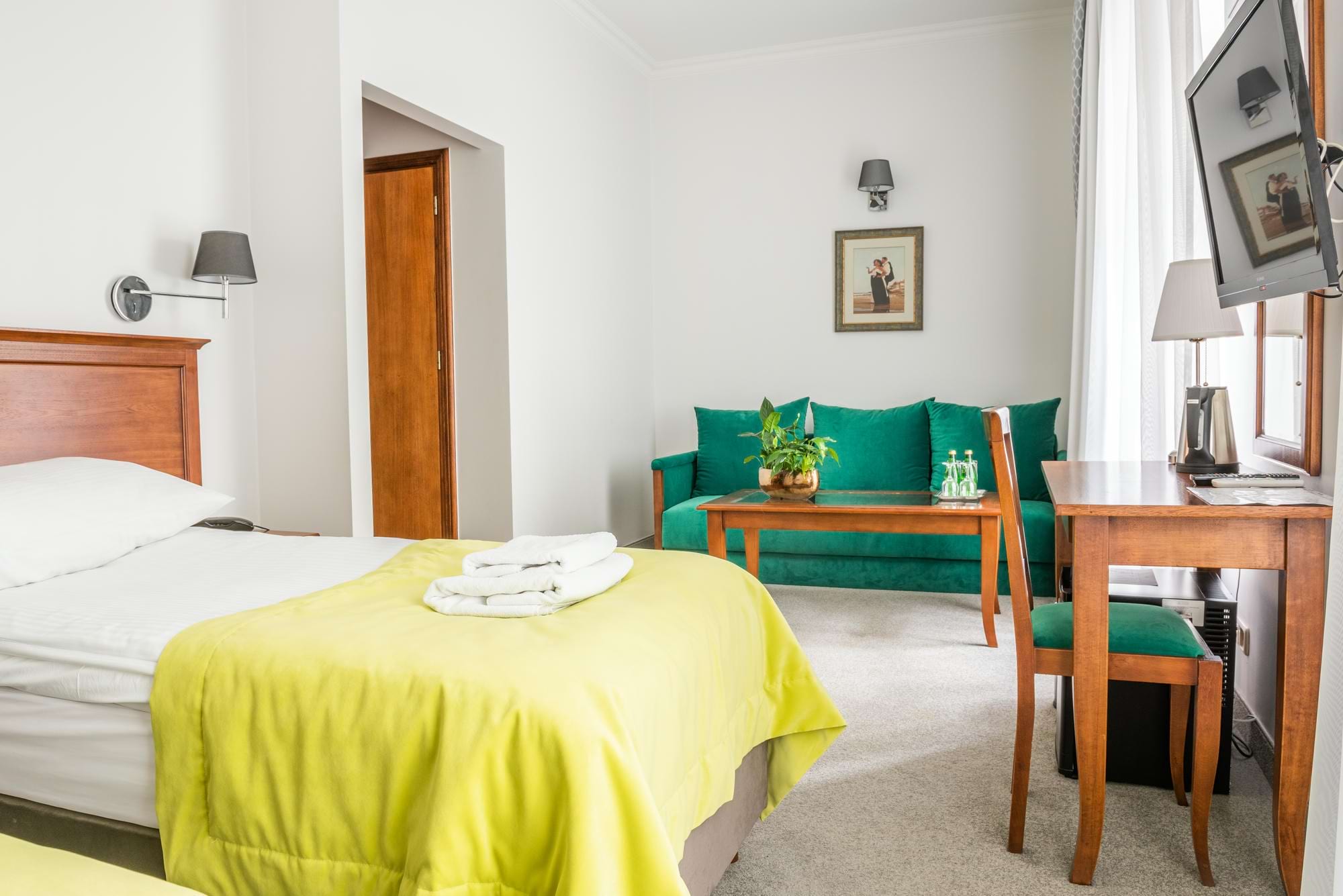 Pokój hotelowy z łóżkiem, żółtozieloną narzutą, zieloną sofą i rośliną