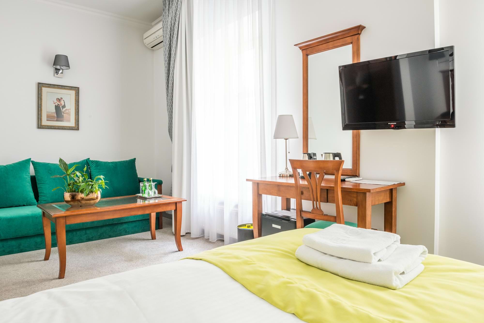 Pokój hotelowy z zieloną sofą, żółtą pościelą i telewizorem