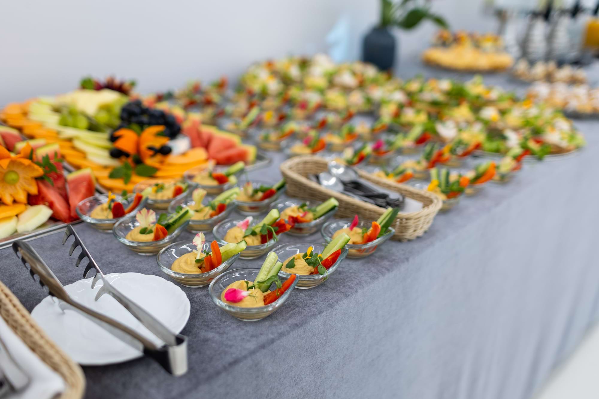 Stół z przekąskami, mini miseczki z pastą i warzywami, owoce w tle