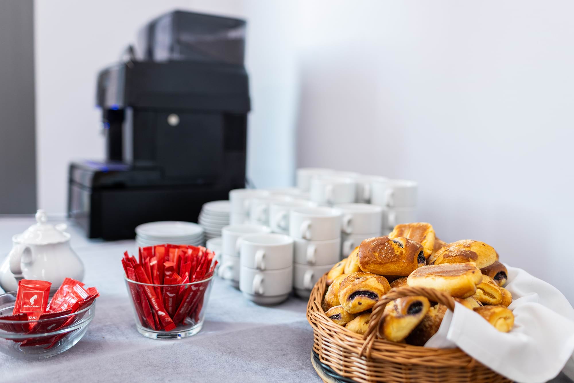 Ekspres do kawy w tle, kubki, cukier w saszetkach, kosz rogalików