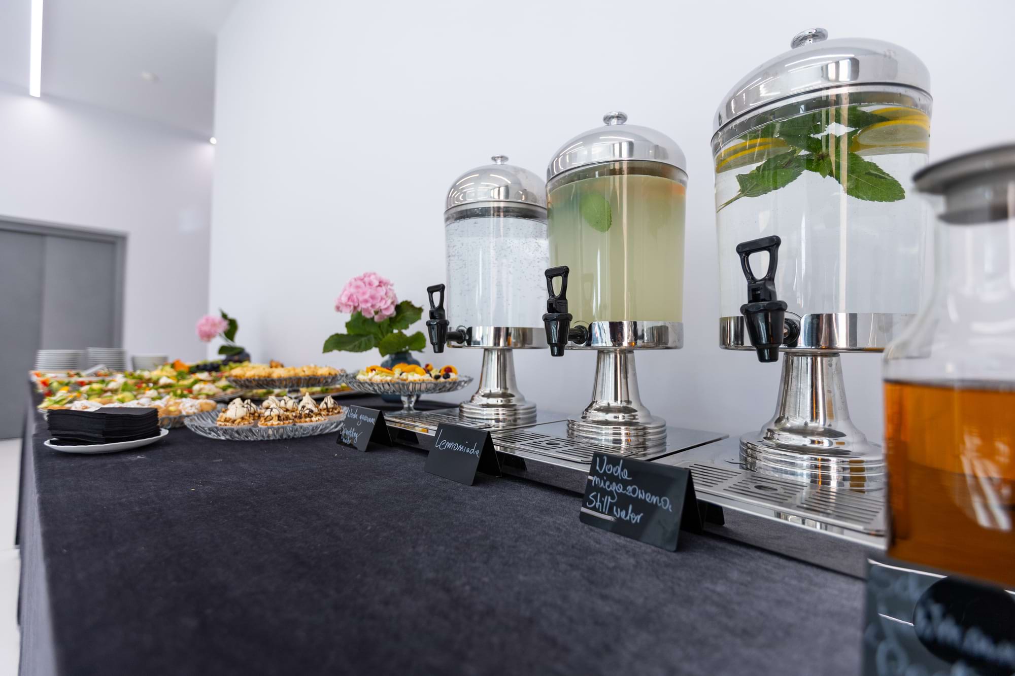 Trzy szklane dystrybutory z napojami na stojakach przy bufecie