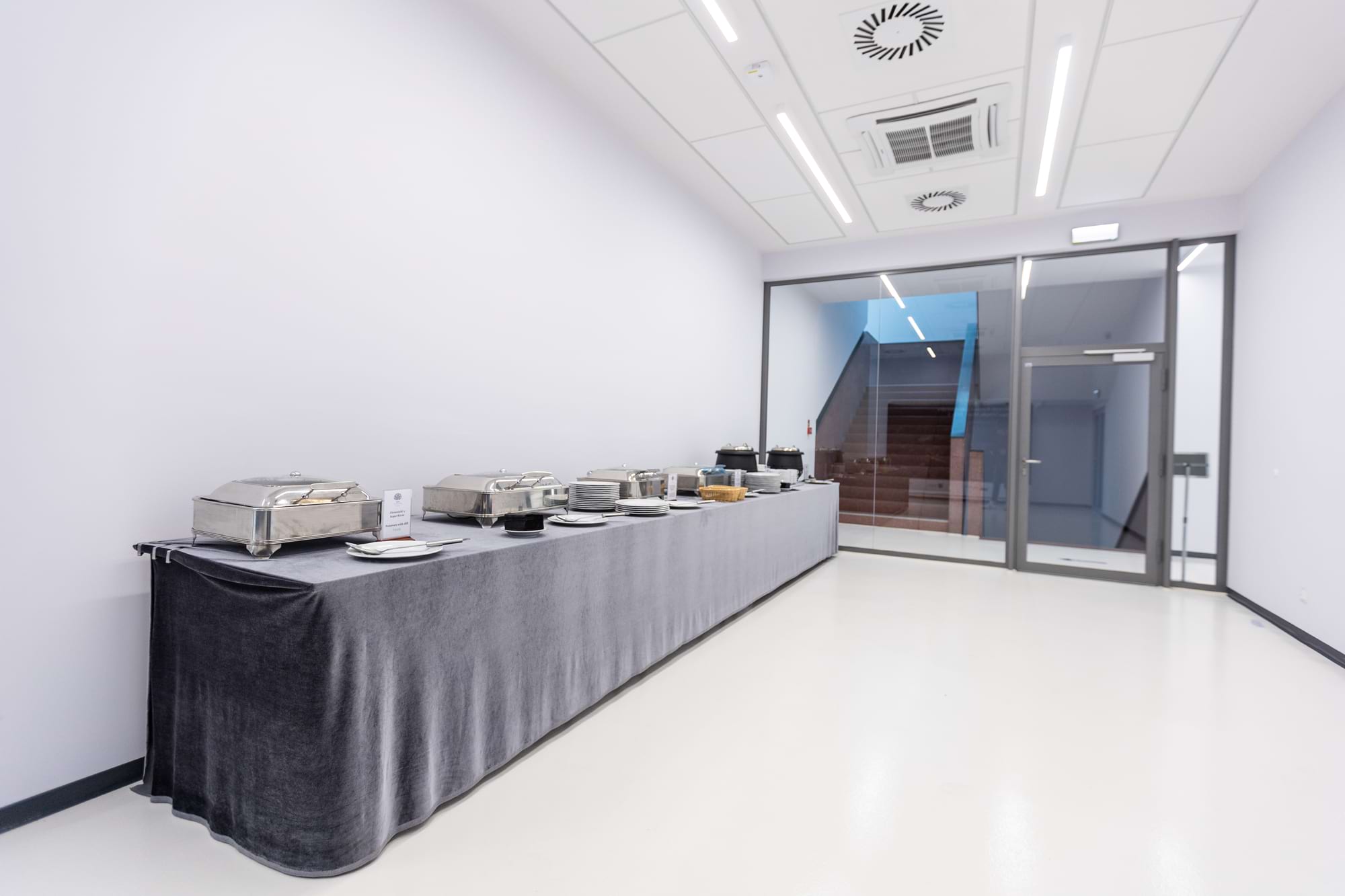 Długi bufet z metalowymi naczyniami na szarym obrusie w jasnym holu