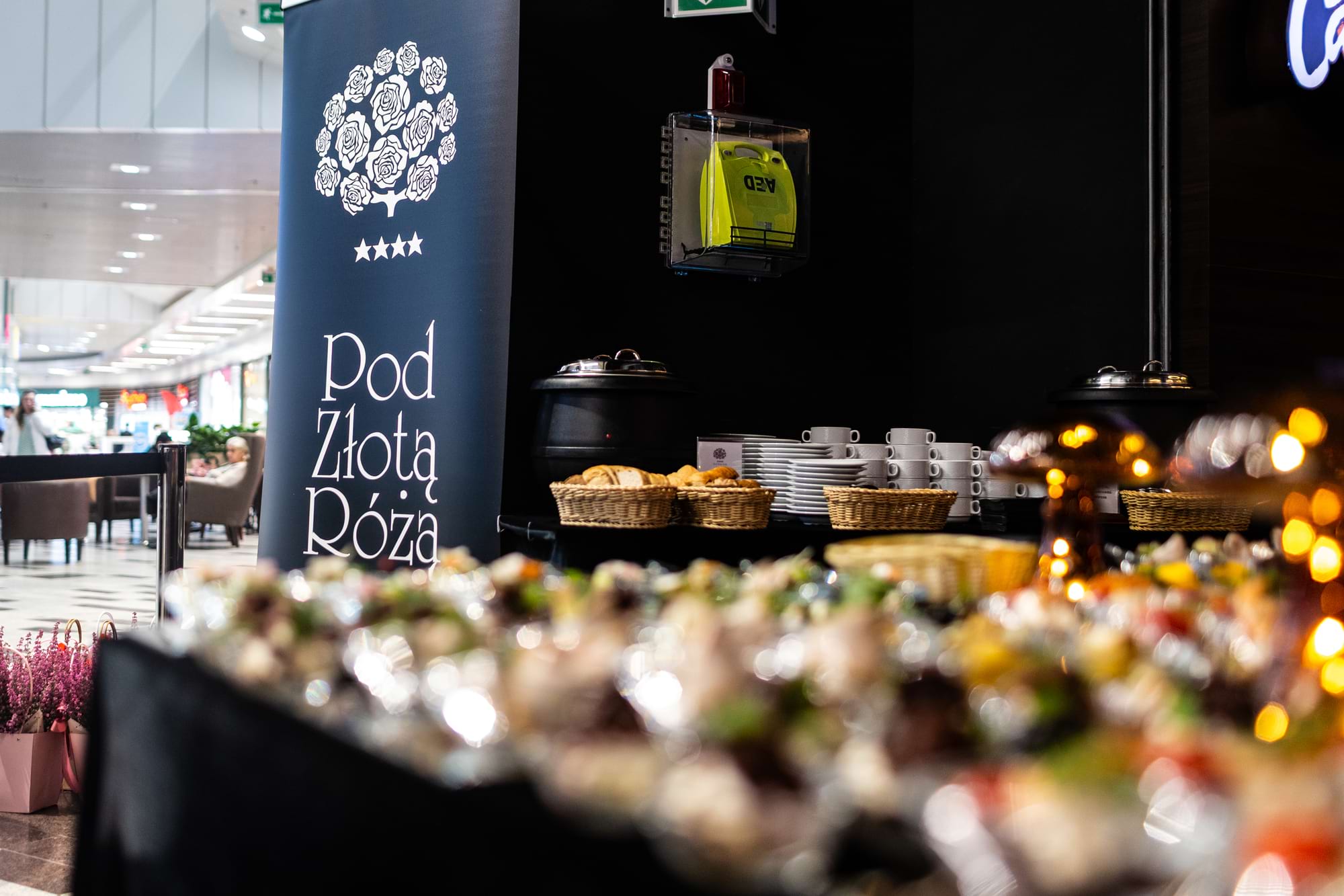 Słup reklamowy Pod Złotą Różą przy stolikach z chlebem i filiżankami