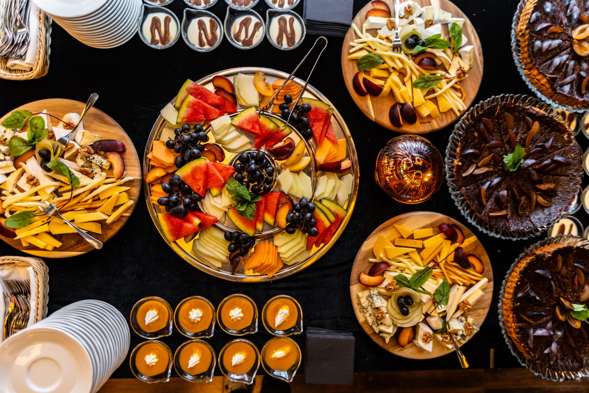 Stół z przekąskami: owoce, sery i ciasta na czarnym stole