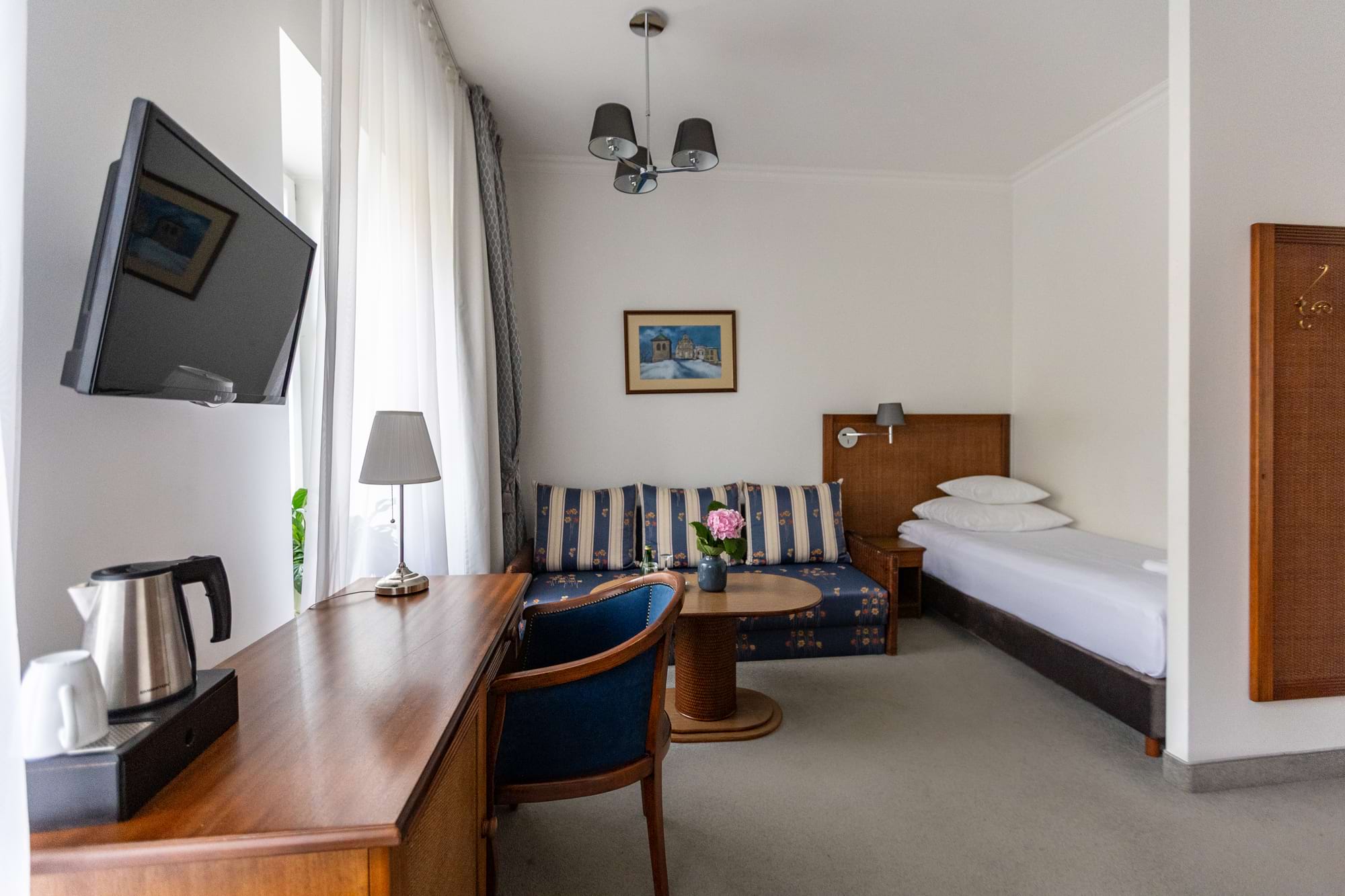 Pokój hotelowy z niebiesko-beżową sofą w paski, łóżkiem i telewizorem